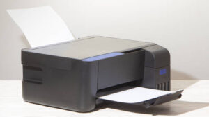 Black desktop printer on a wooden surface with paper loaded for printing.